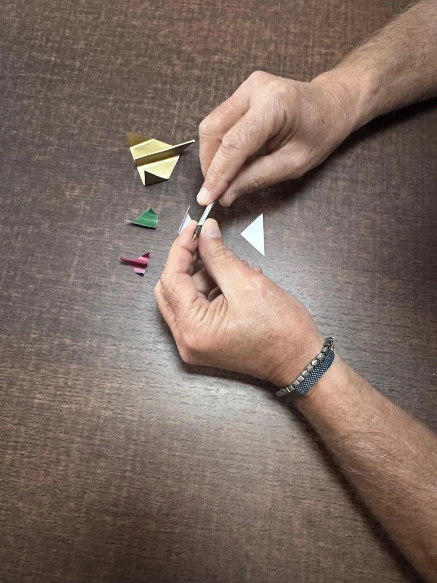 Le mani di Giuseppe sagomano un triangolo d’alluminio con un piccolo attrezzo, accanto ad altri triangoli già piegati